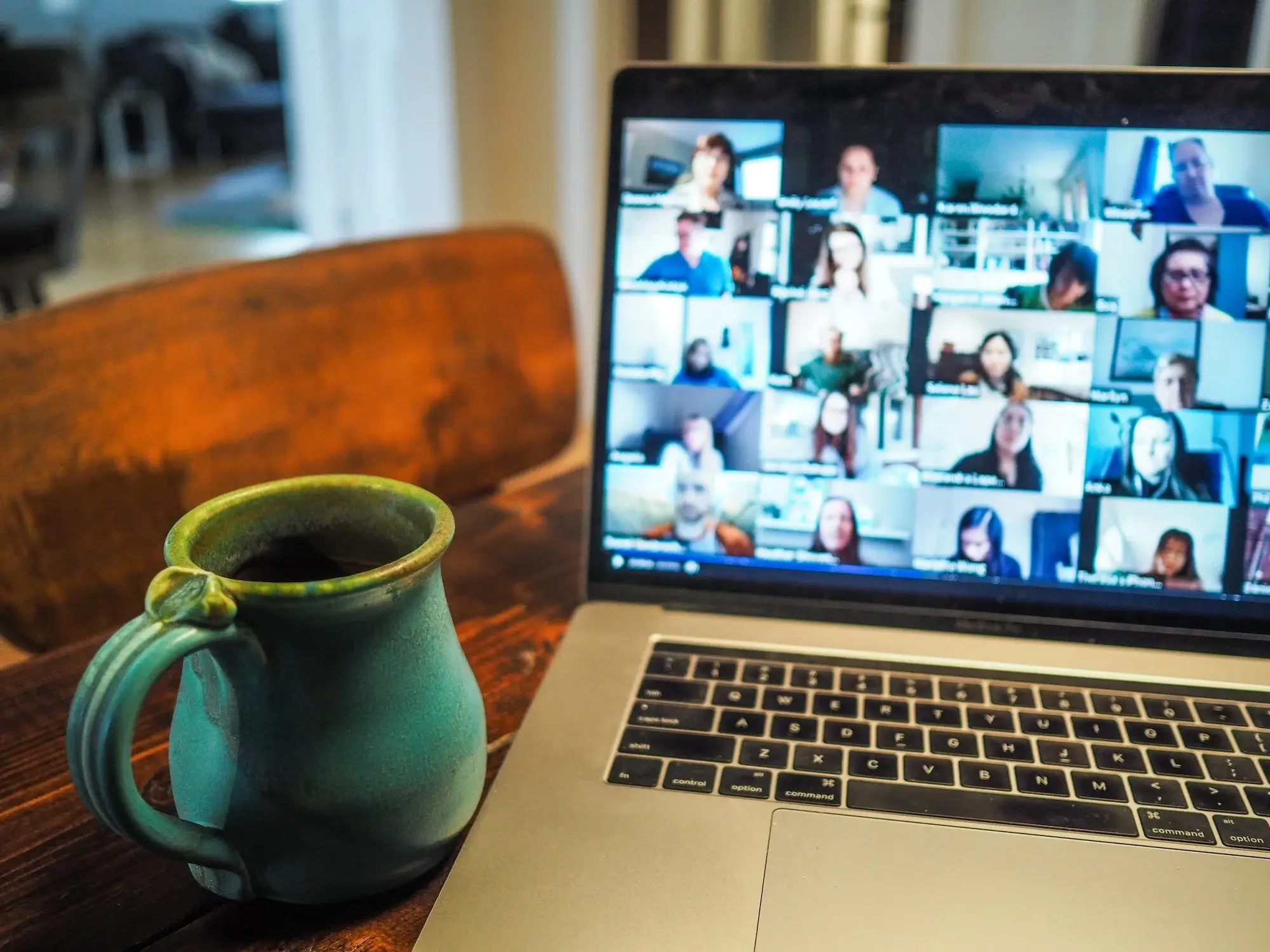 green mug beside a macbook with a virtual meeting for remote work