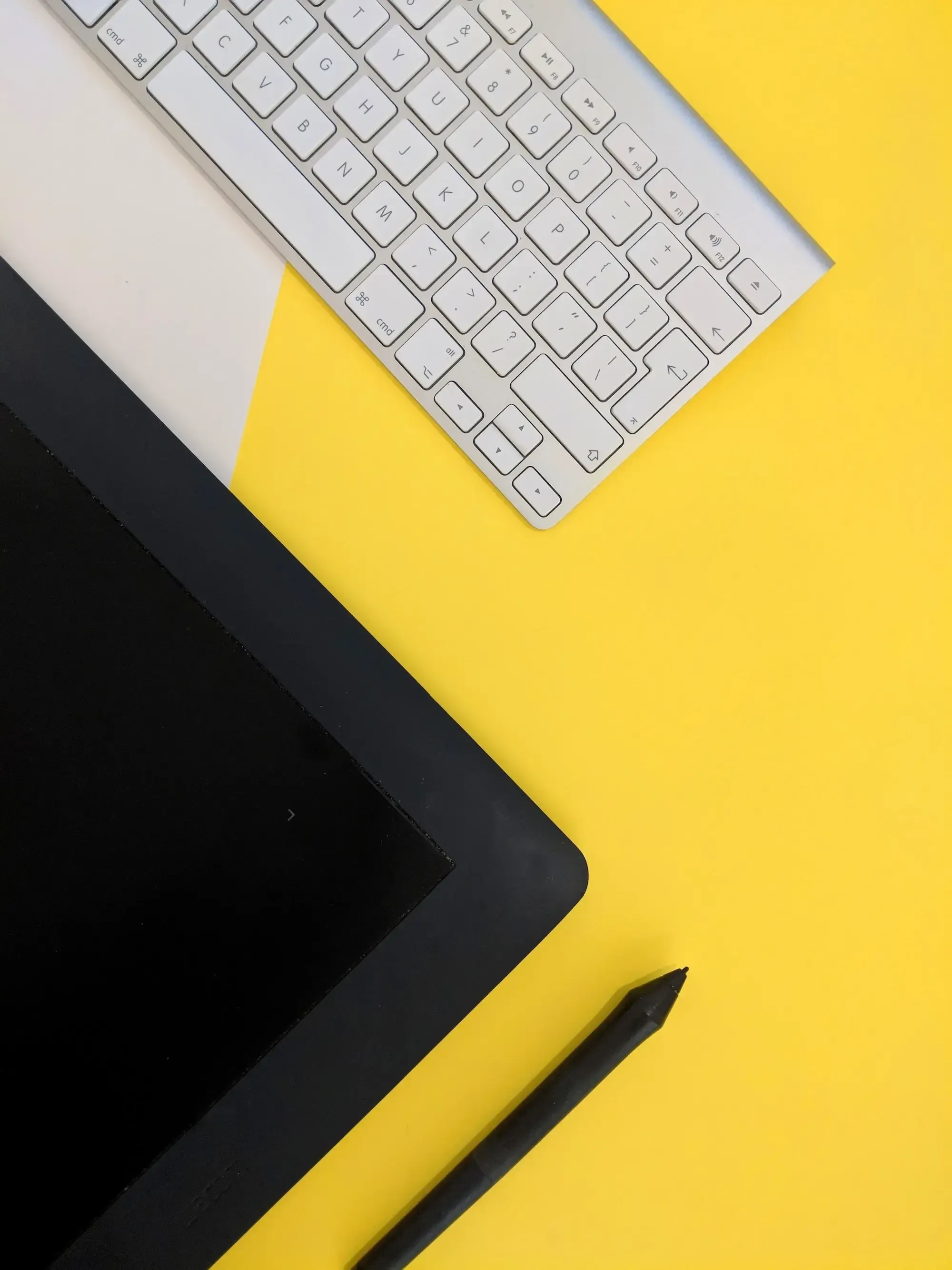 Black tablet, black pen and white keyboard on yellow background. 