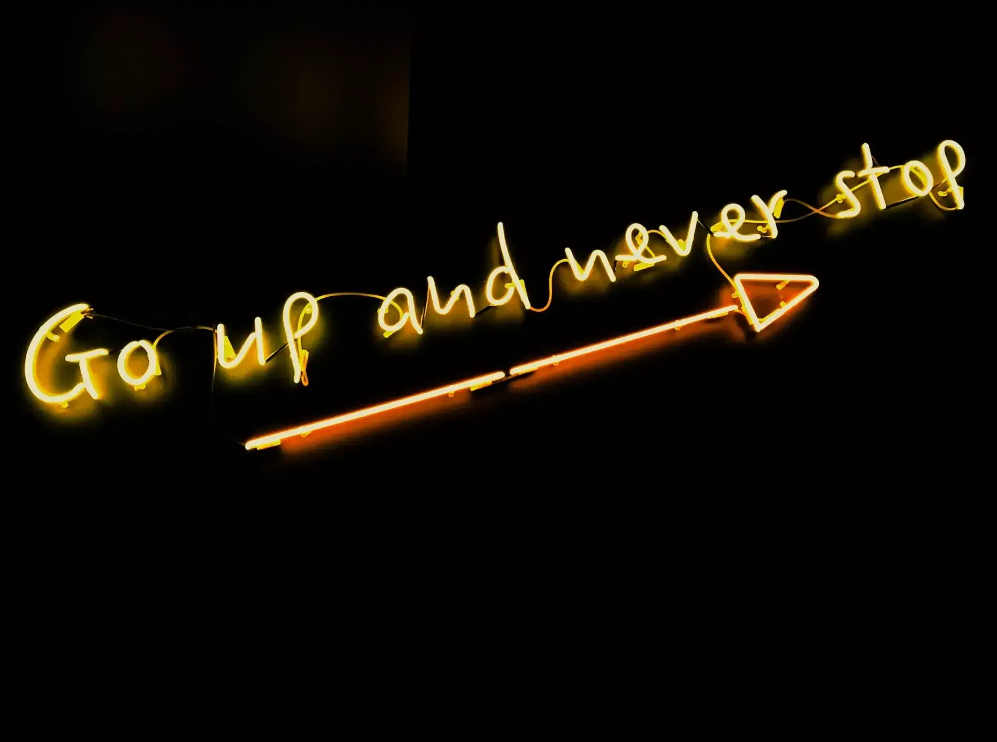 "Go up and never stop" in yellow illuminated lettering on a black background. 