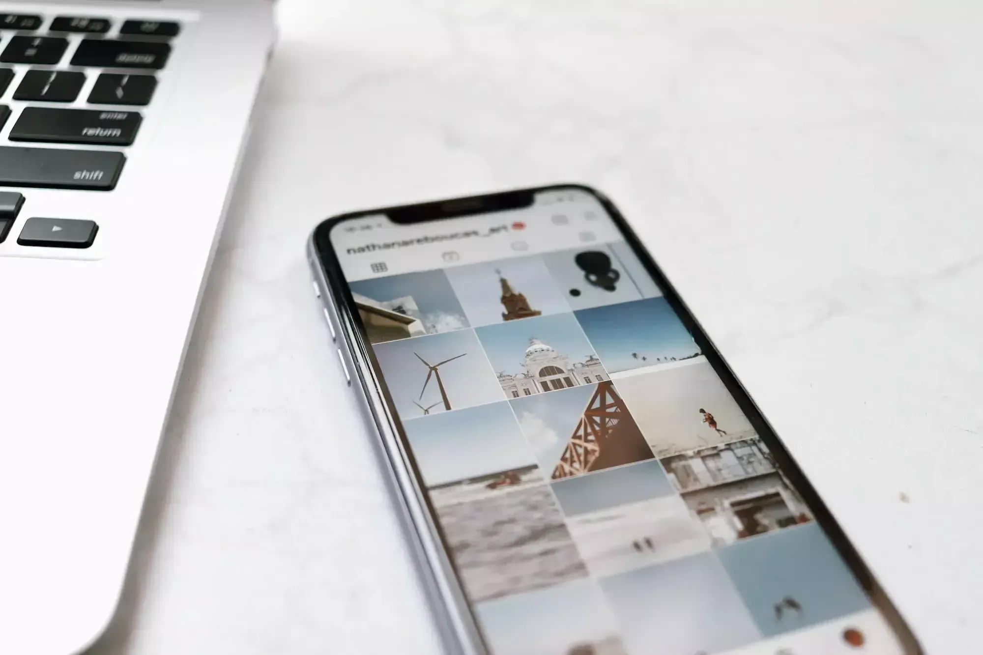 iPhone auf einem weißen Tisch neben MacBook, darauf ein Instagram-Profil mit Architekturbildern.