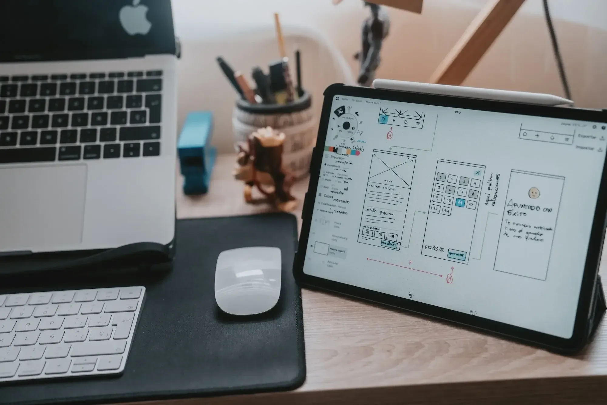 Arbeitsplatz mit Macbook, Tablet, Maus und Tastatur, Tacker, Stifthalter, das Tablet im Zentrum, auf dem Screen ein Product Design Portfolio Entwurf
