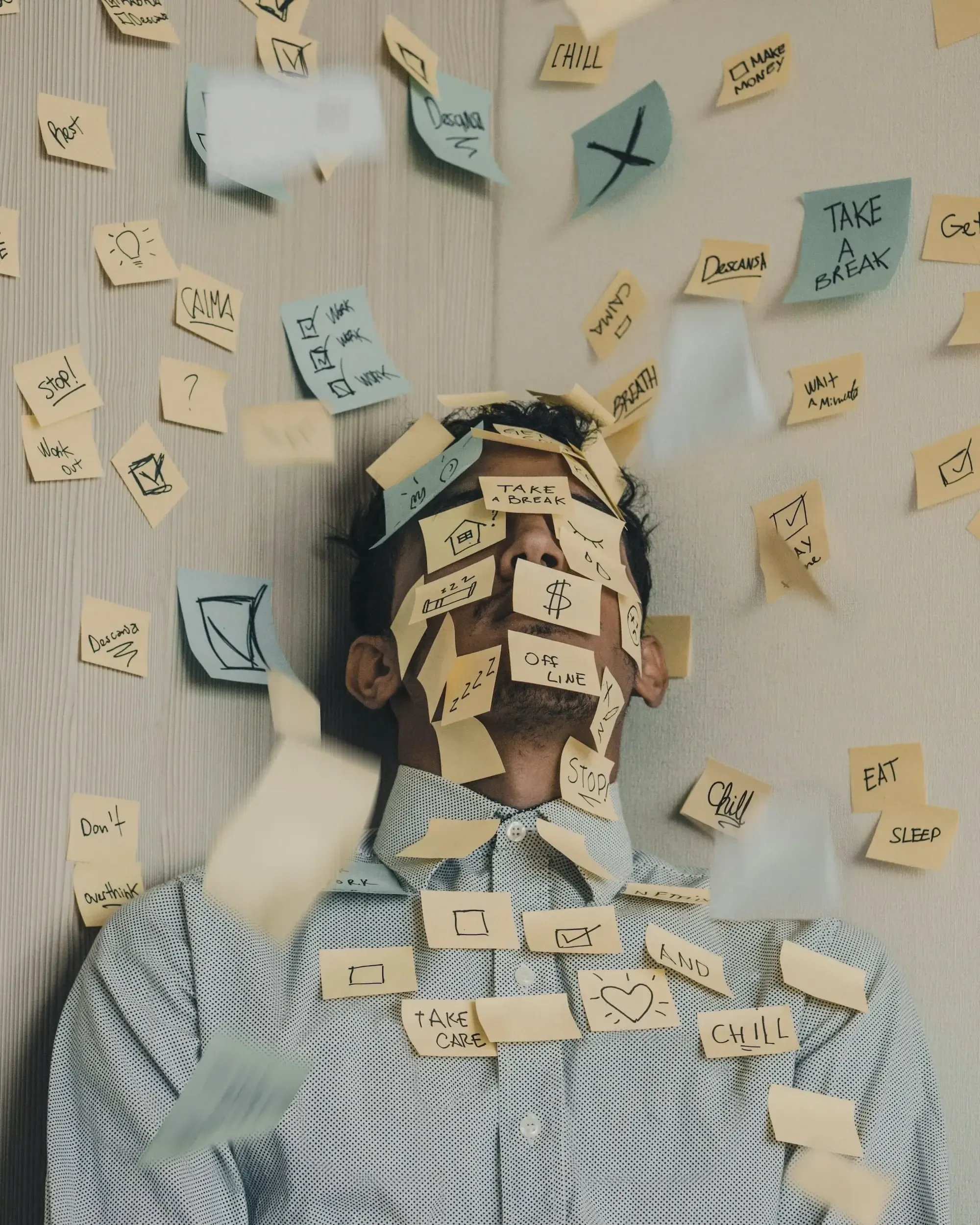 Man in a dotted shirt covered in and surrounded it flying yellow and blue post-its with notes and doodles on them. 