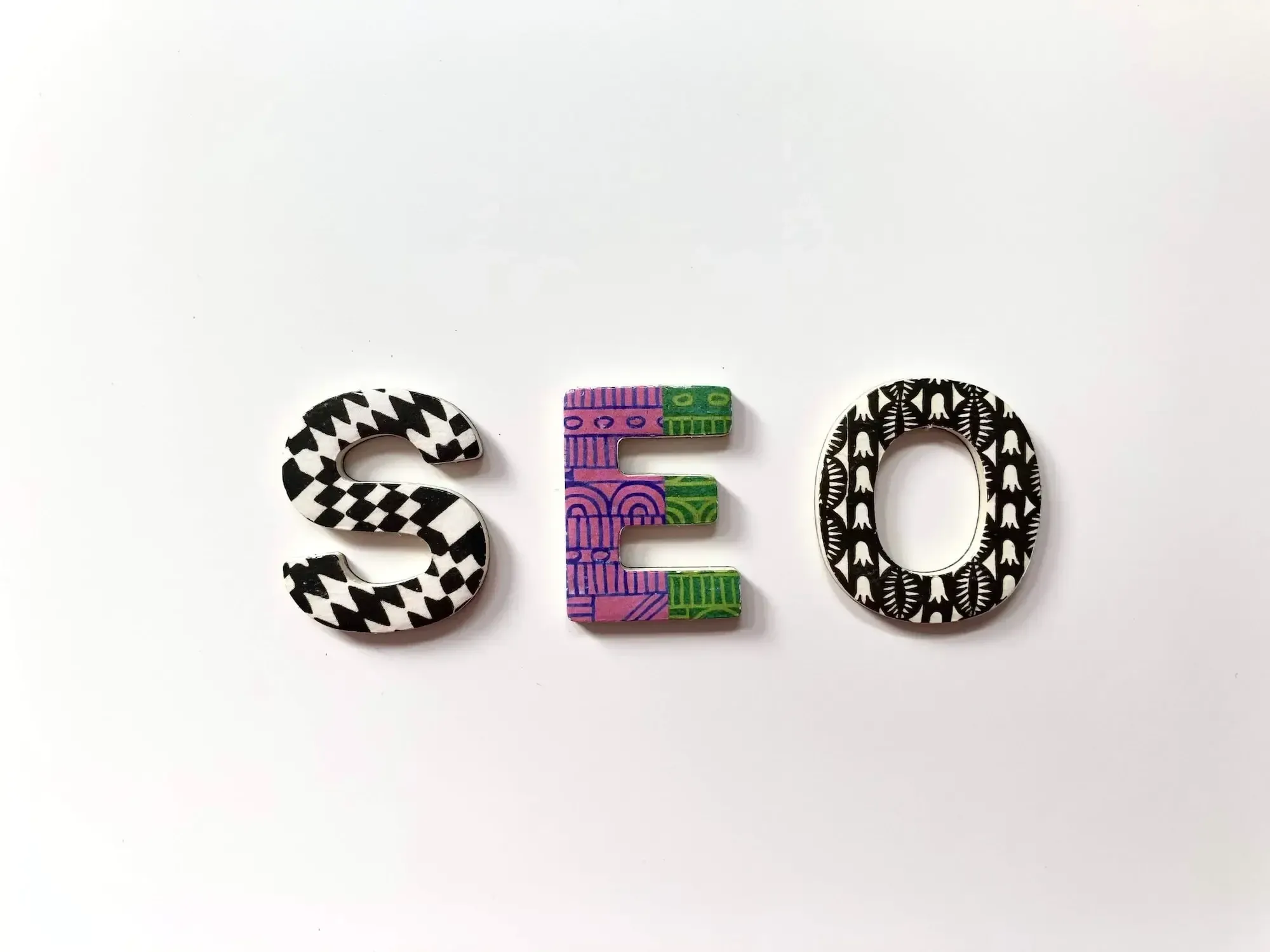 Weißer Hintergrund, drei Buchstaben mit unterschiedlichen Mustern und Farben, die "SEO" buchstabieren.