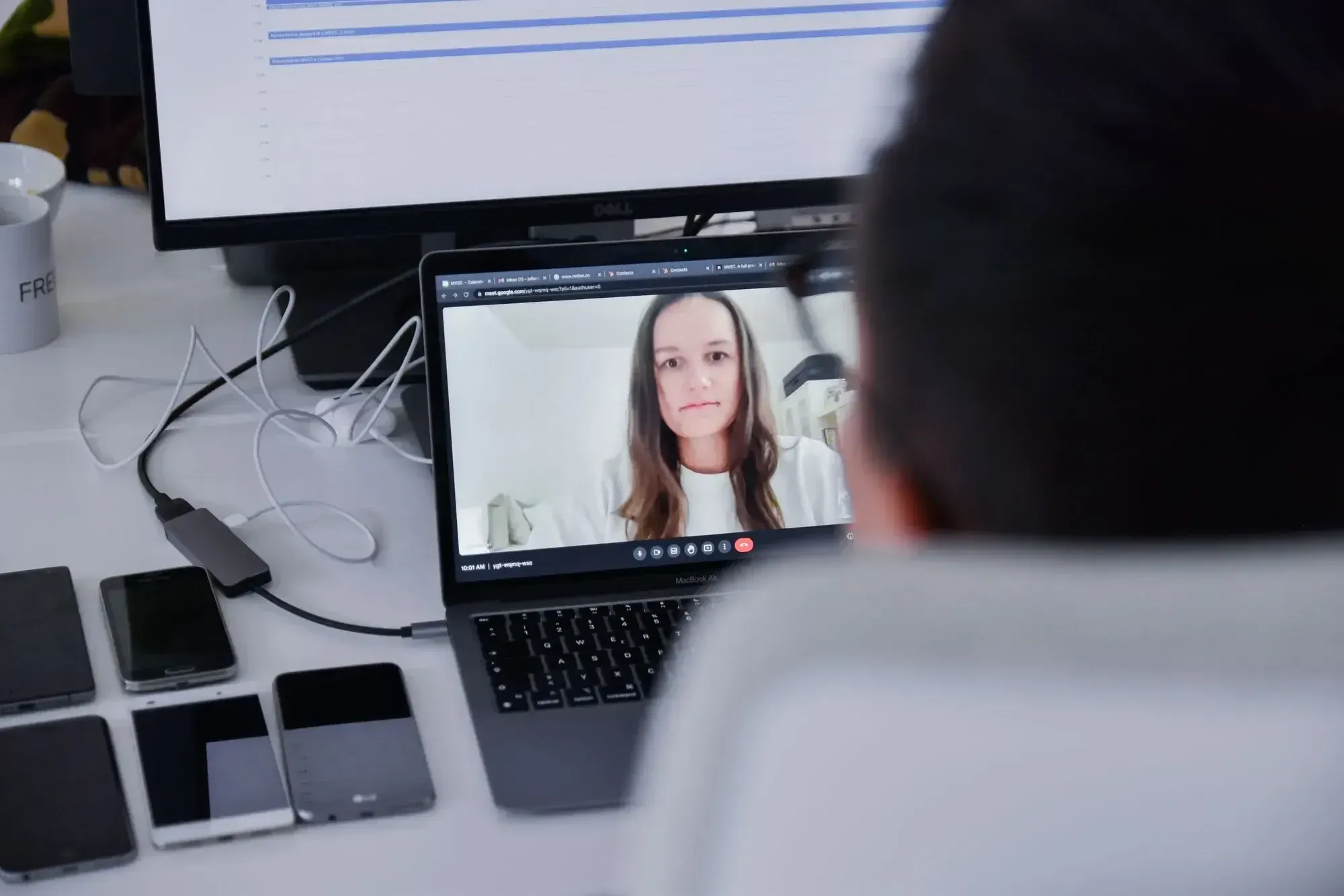 Frau mit langen braunen Haaren in einem virtuellen Meeting auf einem Laptop-Bildschirm, daneben fünf Smartphones.