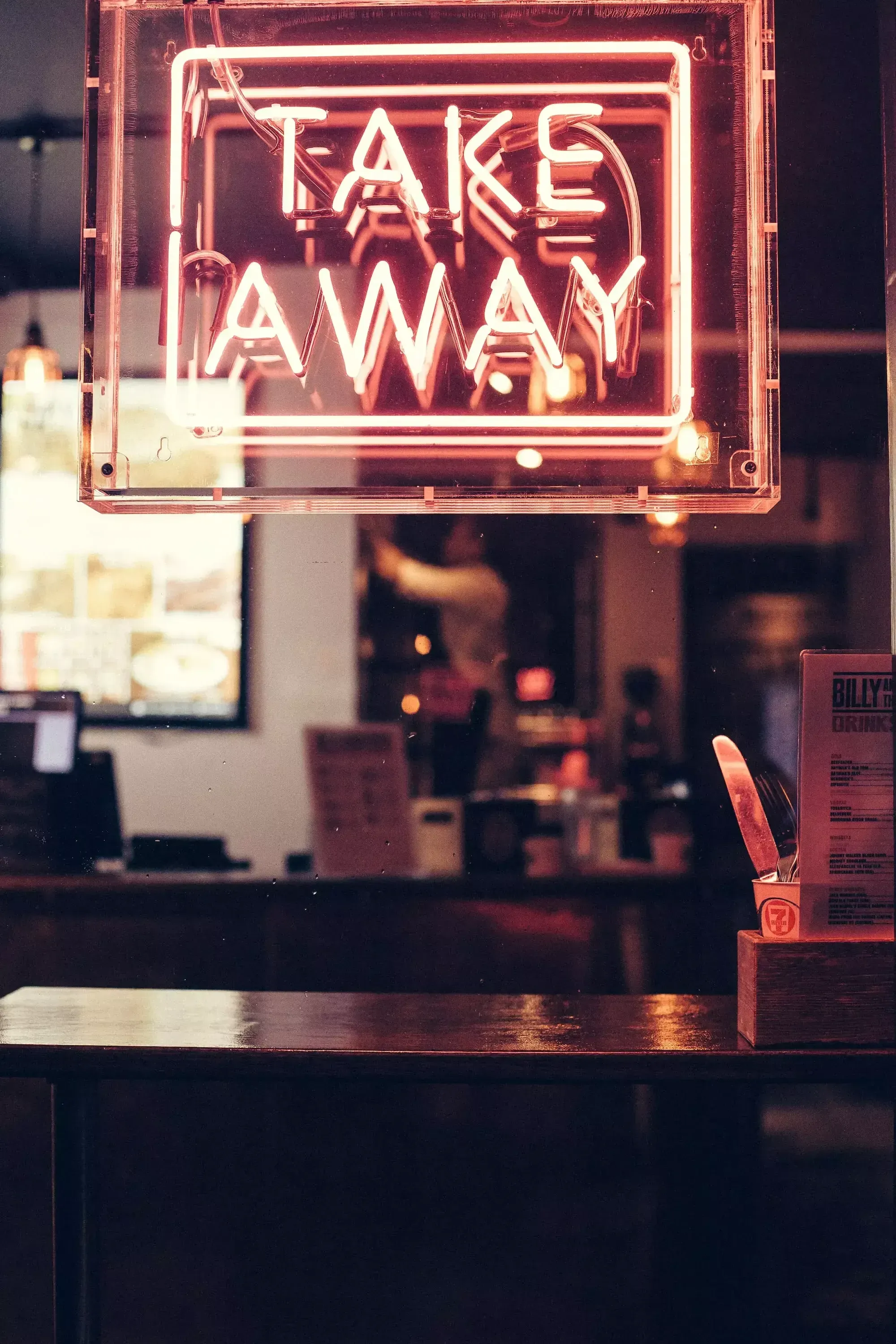 Restaurant-Theke, darüber ein Schild in Leuchtschrift mit "TAKE AWAY" in rotem Licht.
