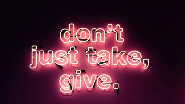 "don't just take, give." in rosa Leuchtschrift an einer dunkelgrauen Wand